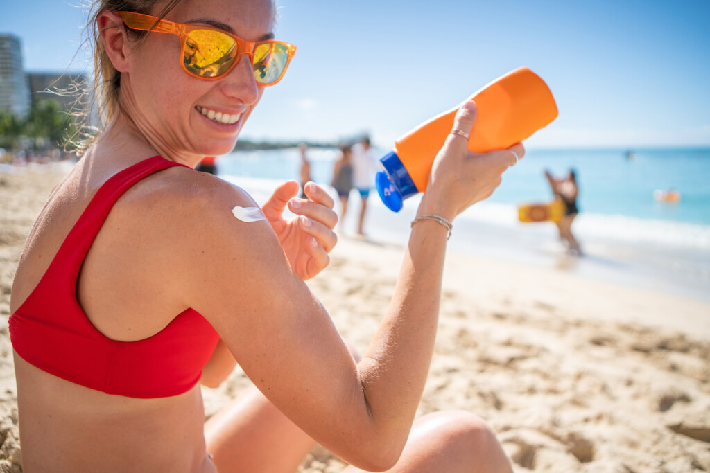 Woman On Beach Applying Sunscreen