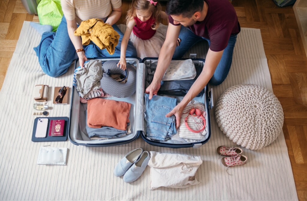 Unrecognizable Family Of Three Sitting On The Floor And Packing Their Suitcase To Go On The Vacation